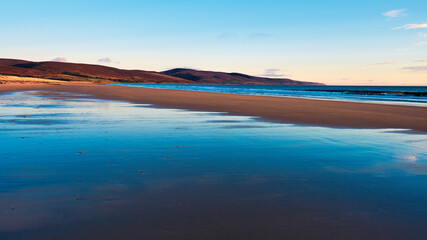 Fototapeta na wymiar Brora beach in the Highlands of Scotland with blue skies and reflections in the wet sand