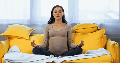 Pregnant woman meditating on couch at home