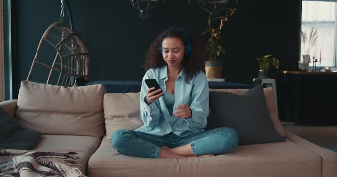 Music streaming app. Beautiful young happy African American student woman listening, dancing to music in headphones.