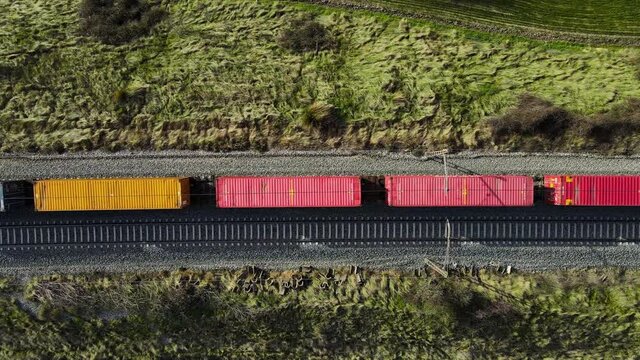 Aerial top view of the freight train, carrying colorful containers, moving through the forest at sunset. 4K footage from drone. High quality 4k footage