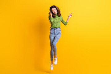 Fototapeta na wymiar Full size photo of brown wavy haired girl wear green sweater jeans point empty space isolated on yellow color background