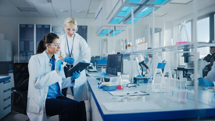 Modern Medical Research Laboratory: Two Female Scientists Working Using Digital Tablet, Analysing...