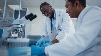 Modern Medical Research Laboratory: Two Smiling Male Scientists Working Together Using Microscope,...