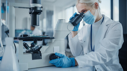 Modern Medical Research Laboratory: Portrait of Female Scientist Wearing Face Mask Looking Under Microscope, Analysing Test Samples. Advanced Scientific Lab for Medicine, Microbiology Development