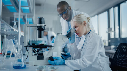Modern Medical Research Laboratory: Two Scientists Working Together Using Microscope, Analysing Samples, Talking. Advanced Scientific Lab for Medicine, Biotechnology.