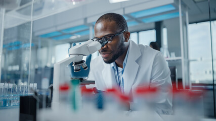 Modern Medical Research Laboratory: Portrait of Male Scientist Looking Under Microscope, Analysing...