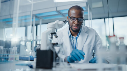 Modern Medical Research Laboratory: Portrait of Male Scientist Using Microscope, Writing Down...