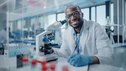 Modern Medical Research Laboratory: Portrait of Male Scientist Using Microscope, Charmingly Smiling...