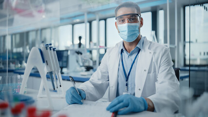 Medical Research Laboratory: Portrait of Male Scientist Wearing Face Mask Looking at Camera, Writing Down Information. Advanced Scientific Lab for Medicine, Biotechnology, Microbiology Development