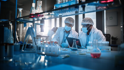 Modern Medical Research Laboratory: Two Scientists Wearing Face Masks use Microscope, Analyse...