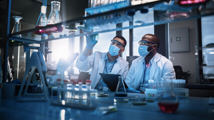 Modern Medical Research Laboratory: Two Scientists Wearing Face Masks use Microscope, Analyse...