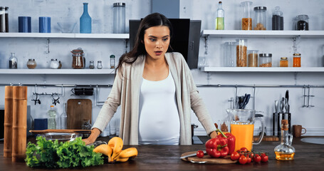 Excited pregnant woman looking at fresh ingredients on kitchen table
