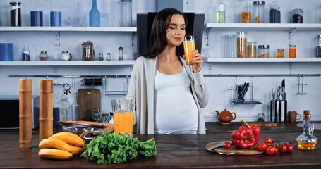 Pregnant woman holding glass of orange juice near vegetables and bananas