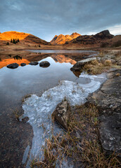 Beautiful Winter morning at Blea Tarn in the English Lake District with golden light on the mountains and perfect reflections in the water.