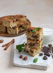 Oatmeal squares with chocolate and a cup of milk, light concrete background. Diet bars. Healthy bakery for breakfast or dessert.