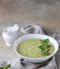 Vegetarian cream soup of green vegetables (broccoli, green peas, spinach) served with mint and seeds on concrete background. Clean eating, healthy food concept.
