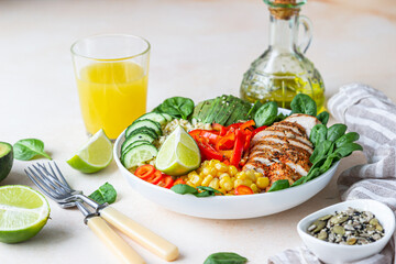 Healthy buddha bowl lunch with grilled chicken and bulgur, spinach, avocado, cucumber, bell pepper and corn on light background. Delicious balanced food concept.