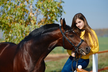 Obraz premium Young female farmer taking care about horse on ranch on summer day, copy space. Girl stroking and hugging brown horse