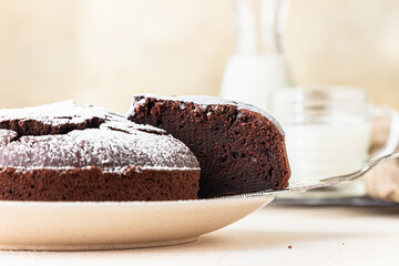 Chocolate sponge flourless cake with sugar powder, light concrete background. Brownie cake. Toned image.