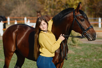 Young female farmer taking care about horse on ranch on summer day, copy space. Girl stroking a brown horse