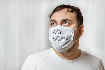 a man in a white protective medical mask looks up. Stay at home mask lettering