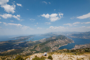 Fototapeta na wymiar A man and a woman are sitting in an embrace on a bench, a panoramic view of the Bay of Kotor opens in front of them 