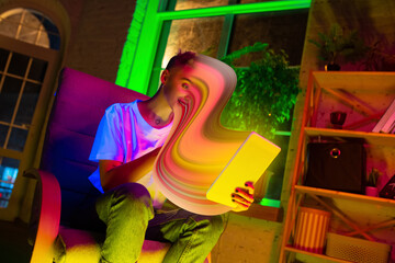 Cinematic portrait of stylish woman in neon lighted interior using a tablet. The face is smeared, sucked, absorbed into the screen. Concept of social network dependency, phone addiction.