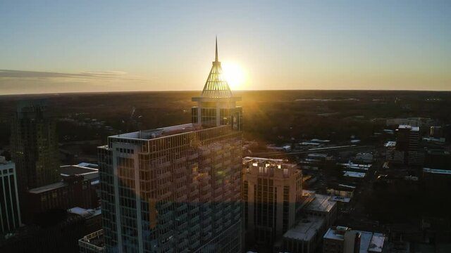 Sunset at the horizon disappearing after the top pirmide of a skyscraper build from glass in downtown Raleigh on a bright sunny summer day. Wide Drone dolly shot