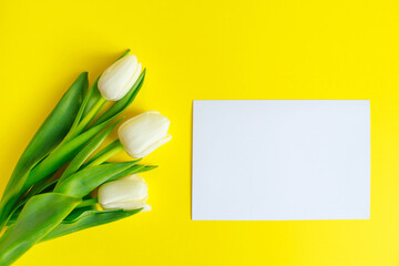 White tulips bouquet and greeting card on a yellow background. Spring holidays concept, mockup.