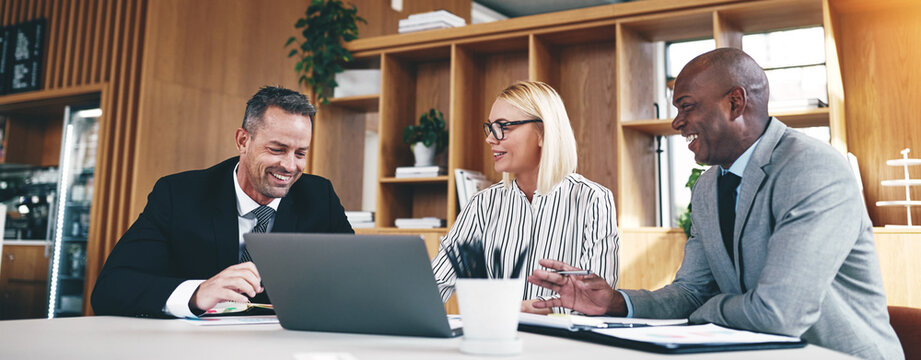 Three diverse businesspeople laughing while working together in an office