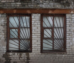 Two windows covered with rusty metal bars in an old white brick wall