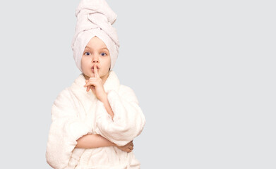 Beauty child girl face portrait. Beautiful model girl with perfect fresh clean skin in white towel making silence sign Isolated on white background. Youth and skin care concept. 