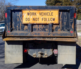 Rear view of muddied and rusty industrial truck with WORK VEHICLE DO NOT FOLLOW sign.
