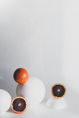 Fototapeta na wymiar Creative still life with red orange fruits and white geometric shapes, spheres. Modern minimal composition with copy space