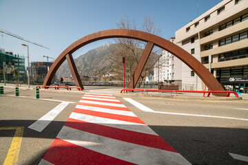 Obraz premium white and red pedestrian crossing seen in perspective passing under the rusty metal arch in the city