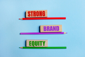 On a blue background, three colored pencils, three wooden blocks with text STRONG BRAND EQUITY