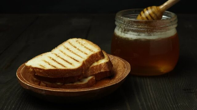 slices of bread dripped with honey in a wooden plate and a jar of honey on a dark wooden background