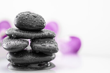 Spa stone tower in a milky liquid with a blurred purple orchid in the background against a white backdrop