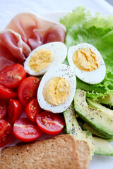 Boiled eggs, bacon, avocado, toast and tomatoes and lettuce salad.