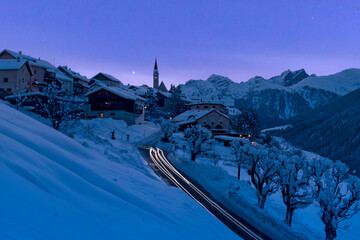 Snow covered village of Guarda lit by car trail lights during a blue winter dusk, Lower Engadine, Graubunden Canton, Switzerland,  Europe