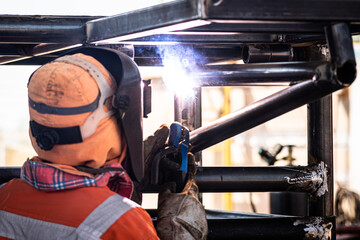 A welder worker is welding on metal steel pipe to fabricate an ironwork construction object. Industrial work action photo, selective focus.