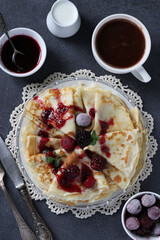 Thin pancakes with wheat flour, eggs and kefir, served with berries, jam and cup of cofee on gray table. View from above