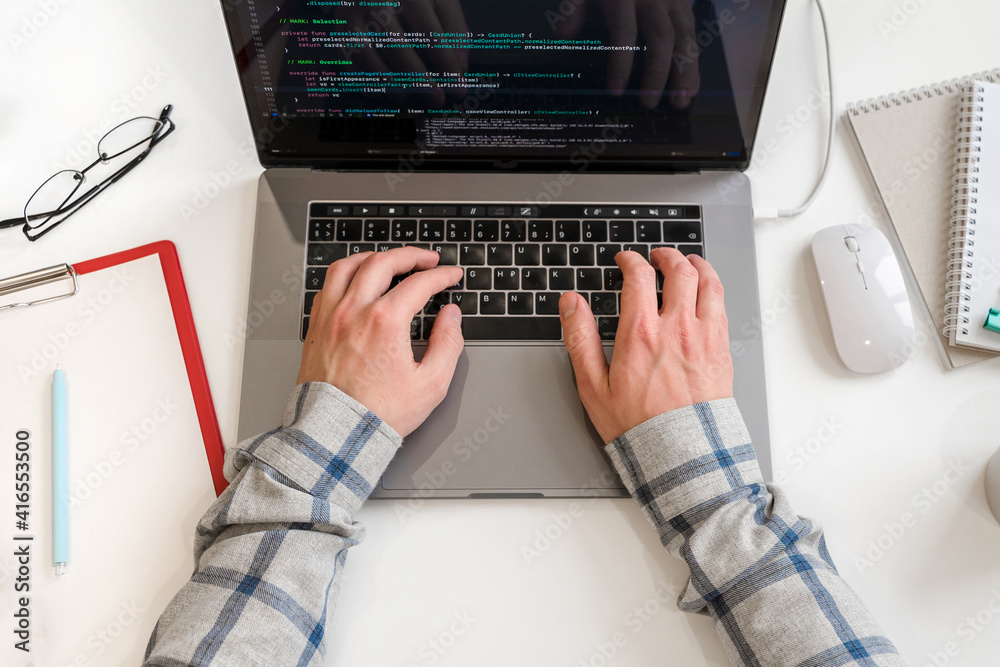 Wall mural a young male programmer uses a laptop and types code in the office. software, programming concept