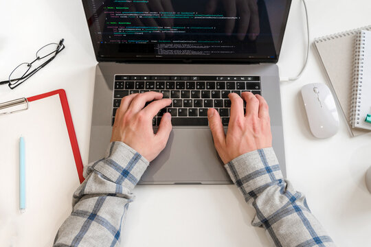 A young male programmer uses a laptop and types code in the office. Software, programming concept