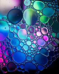 Oil drop bubbles on a water surface abstract with a blue, green and pink background