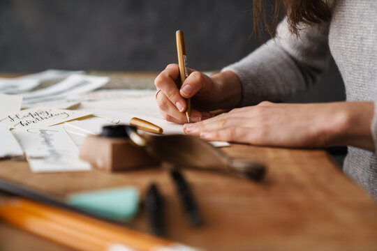 Calligrapher girl writing while working at table indoors - Powered by Adobe