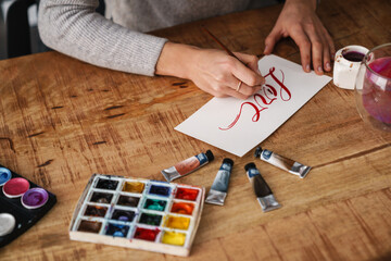 Calligrapher girl writing while working on valentines at table indoors