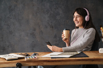 Smiling calligrapher girl using cellphone and drinking coffee