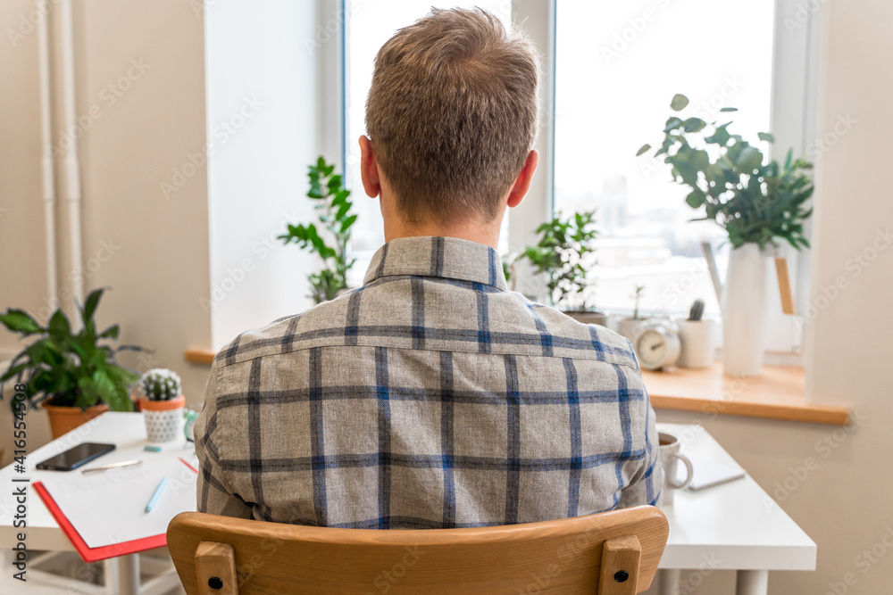 Canvas Prints rear view of a man in a shirt sitting at a desk in front of an office window