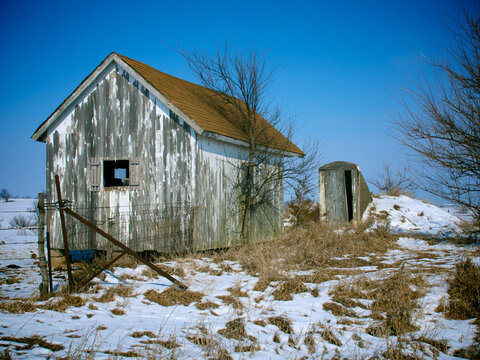 A winter scene of a rural  abandoned shed and storm cellar next to a fence in the snow, near Loeffler, Missouri, 2008
